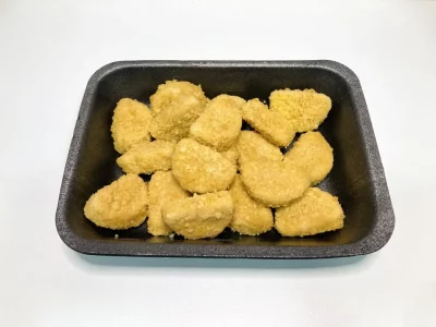 Nuggets de pollo dorados y crujientes, presentados en bandeja negra sobre fondo blanco, listos para servir.