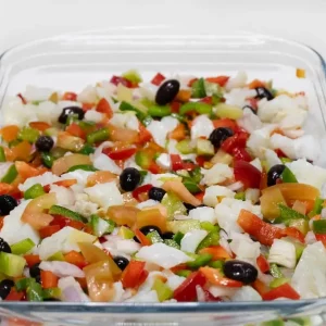 "Plato de esqueixada con bacalao desmigado, tomate y aceitunas, listo para degustar."