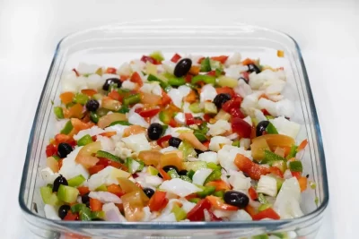 "Plato de esqueixada con bacalao desmigado, tomate y aceitunas, listo para degustar."