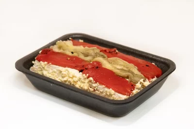 Un pastel de escalivada servido en un plato de cerámica, con su superficie dorada y acompañado de salsa romesco y pan tostado.