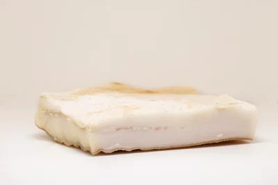 "Porción de tocino blanco fresca, mostrando su textura veteada y su color natural."