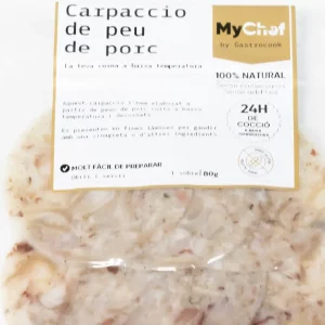 Carpaccio de pies de cerdo en finas láminas, servido con vinagreta y brotes verdes sobre plato blanco.
