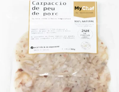 Carpaccio de pies de cerdo en finas láminas, servido con vinagreta y brotes verdes sobre plato blanco.