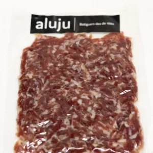Virutas de jamón ibérico cortadas a mano, con vetas de grasa y color intenso, servidas sobre tabla de madera.