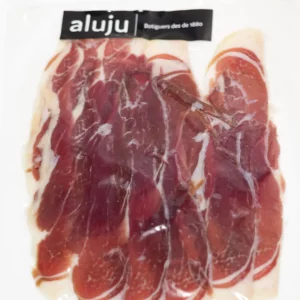 Lonchas finas de jamón ibérico curado, con vetas de grasa infiltrada y color rojo intenso, servidas sobre tabla de madera.