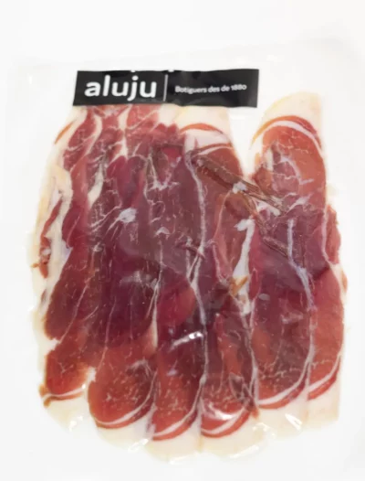 Lonchas finas de jamón ibérico curado, con vetas de grasa infiltrada y color rojo intenso, servidas sobre tabla de madera.