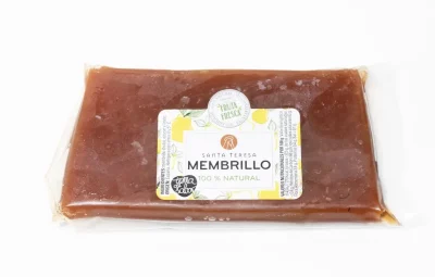 Porción de dulce de membrillo natural, de color ámbar intenso, servida en tabla de madera con cuchillo y fondo rústico.