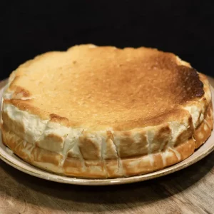 Porción de cheesecake clásica al horno, con base de galleta y cobertura brillante, servida en plato blanco con fondo neutro.