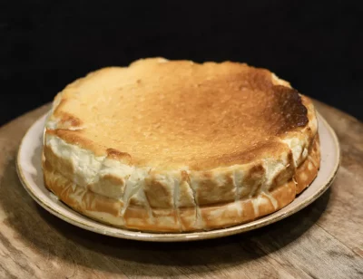 Porción de cheesecake clásica al horno, con base de galleta y cobertura brillante, servida en plato blanco con fondo neutro.