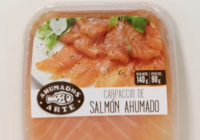 Carpaccio de salmón ahumado en finas lonchas, servido con hojas verdes y aliño de aceite y pimienta sobre plato blanco.
