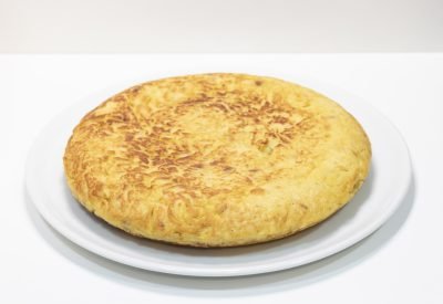 Tortilla de patatas sin cebolla, dorada por fuera y jugosa por dentro, servida en porciones sobre plato rústico.
