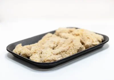 Cabrito rebozado Aluju: tradición, sabor y textura crujiente en cada bocado Bandeja negra con piezas de cabrito rebozado Aluju crudas, cubiertas de pan rallado, listas para freír, sobre fondo blanco.