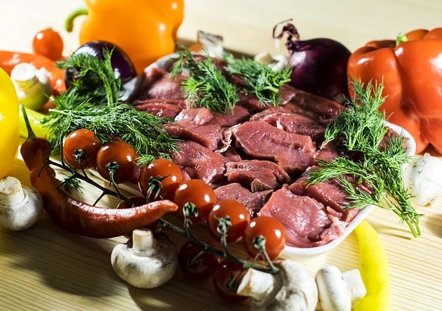 Plato de cabrito crudo Aluju sobre fondo rústico, acompañado de verduras frescas como tomates, pimientos, cebolla y champiñones, listo para preparar guisos o asados tradicionales.