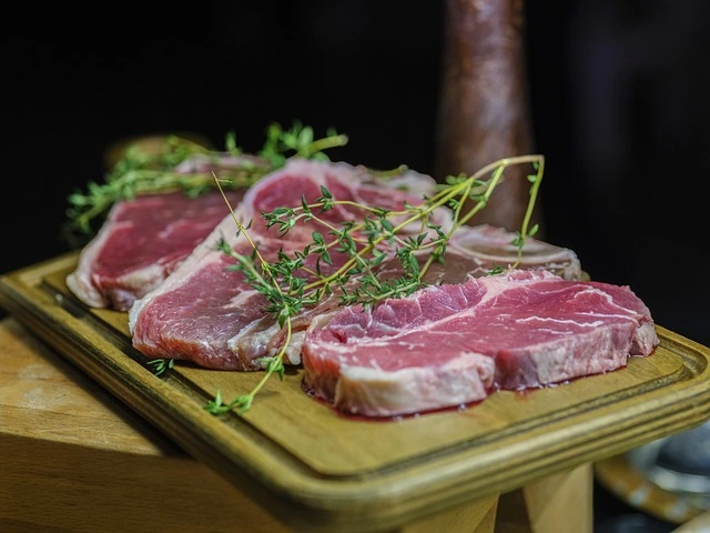 Chuletas de cerdo Aluju crudas sobre tabla de madera, decoradas con tomillo fresco, listas para cocinar a la plancha, horno o barbacoa.