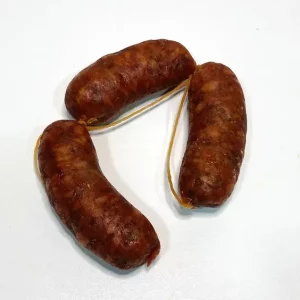 Tres piezas de chorizo Aluju curado, unidas por cuerda, con color rojizo intenso y textura arrugada, sobre fondo blanco.