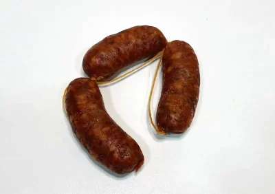 Tres piezas de chorizo Aluju curado, unidas por cuerda, con color rojizo intenso y textura arrugada, sobre fondo blanco.