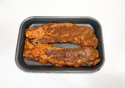 Dos tiras de churrasco adobado Aluju, con color rojizo y especias visibles, presentadas en bandeja negra, listas para cocinar a la parrilla, sartén o al horno.