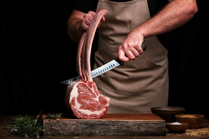 Hombre cortando carne fresca sobre una tabla de madera, con precisión y técnica profesional en nuestra tienda online.
