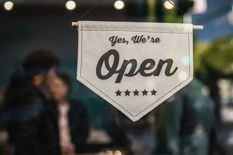 Cartel “Yes, We're Open” con cinco estrellas, colgado en una ventana, transmite apertura y buena atención al cliente.