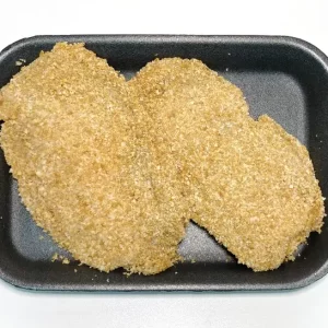 Libritos de pollo Aluju: relleno cremoso en formato crujiente Dos libritos de pollo empanados, dorados y crujientes, presentados en bandeja negra, listos para freír o cocinar al horno.