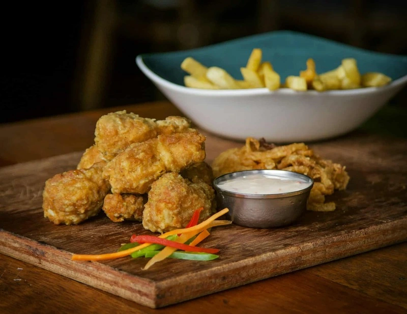 Plato infantil especial niños con tiras de pollo crujiente, salsa para mojar, verduras de colores y patatas fritas, presentado de forma atractiva y divertida.