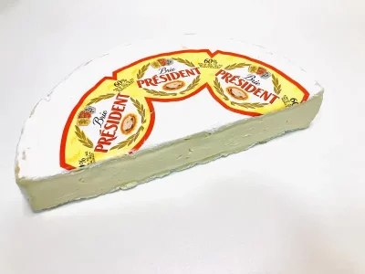 Cuña de queso Brie Président con corteza blanca y textura cremosa, presentada en envase con logotipo visible y 60 % de materia grasa.