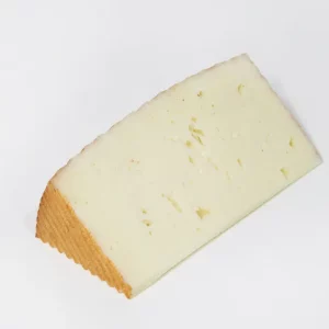 Cuña de queso de cabra bajo en sal, de textura cremosa y color marfil, presentada sobre tabla de madera con fondo neutro.