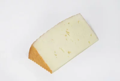 Cuña de queso de cabra bajo en sal, de textura cremosa y color marfil, presentada sobre tabla de madera con fondo neutro.