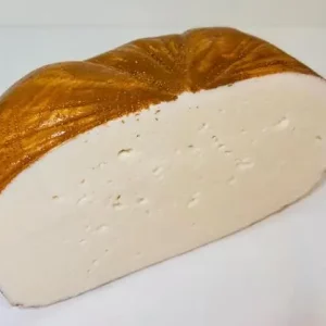 Queso de cabra puro Aluju: sabor auténtico con carácter artesanal Medio queso de cabra puro Aluju, con corteza dorada y pasta blanca, textura firme y pequeños ojos, presentado en bandeja y listo para cortar.