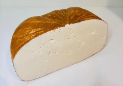 Medio queso de cabra puro Aluju, con corteza dorada y pasta blanca, textura firme y pequeños ojos, presentado en bandeja y listo para cortar.
